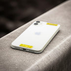 A white phone lying on a stone surface, featuring two yellow AV Edge Cell Phone Protect Filters applied to the back. This EF Technology acts as a signal modulator that might reduce phone radiation without losing signal, potentially helping to reduce phone-induced tech fatigue and brain fog.