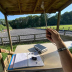 International dressage judge and trainer Alex Gingell wearing the AV Edge Legend White/Black frequency wristband while officiating at an outdoor arena, demonstrating how the HEF Technology might support sustained focus, mental clarity, and posture during long days of high-level judging, offering a non-invasive solution for peak concentration.
