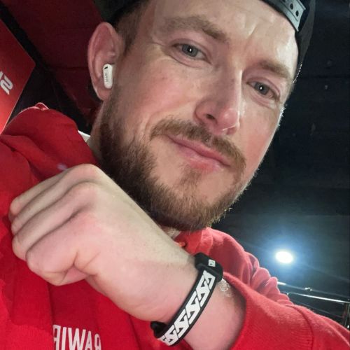 Marcus Mohr golf pro wearing a red hoodie and black cap with a blurred background with his AV Edge Legend Wristband with with EF technology, frequencies, not magnets, that may protect against modern technology EMFs and improve health and performance by stimulating the production of adenosine triphosphate/ATP