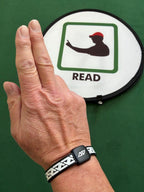Golf coach Mark Bentley wearing the AV Edge Legend White/Black frequency wristband while indicating a 'read' sign, demonstrating how the HEF Technology might support mental focus, green-reading clarity, and balance during instructional sessions, providing a non-invasive tool for peak coaching concentration.