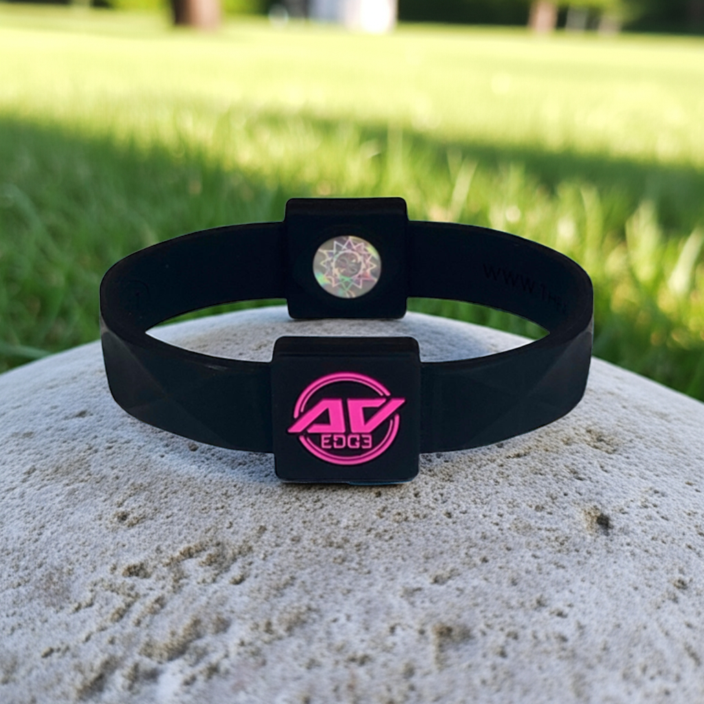 Black and pink AV Edge ADVANCED wristband and bracelet resting on a vibrant autumn leaf, with a softly blurred forest background, suggesting improved performance, balance, and overall health and well-being