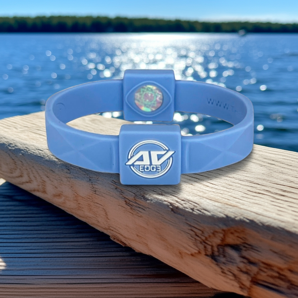 Sky blue AV Edge ADVANCED wristband and bracelet resting on a piece of light driftwood on a wooden dock, with a blurred blue water and summer sky background, symbolizing enhanced energy, focus, and vitality