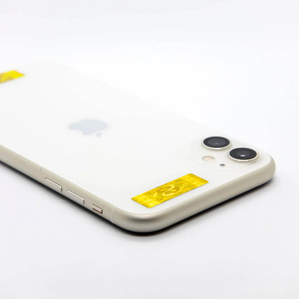 A close-up, angled view of the back of a white iPhone on a plain white background, showing a yellow AV Edge Cell Phone Protect Filter applied near the camera lens. This EF Technology frequency-based filter may help support the user's biofield and reduce tech fatigue by acting as a 4G/5G signal modulator that doesn't compromise device performance.